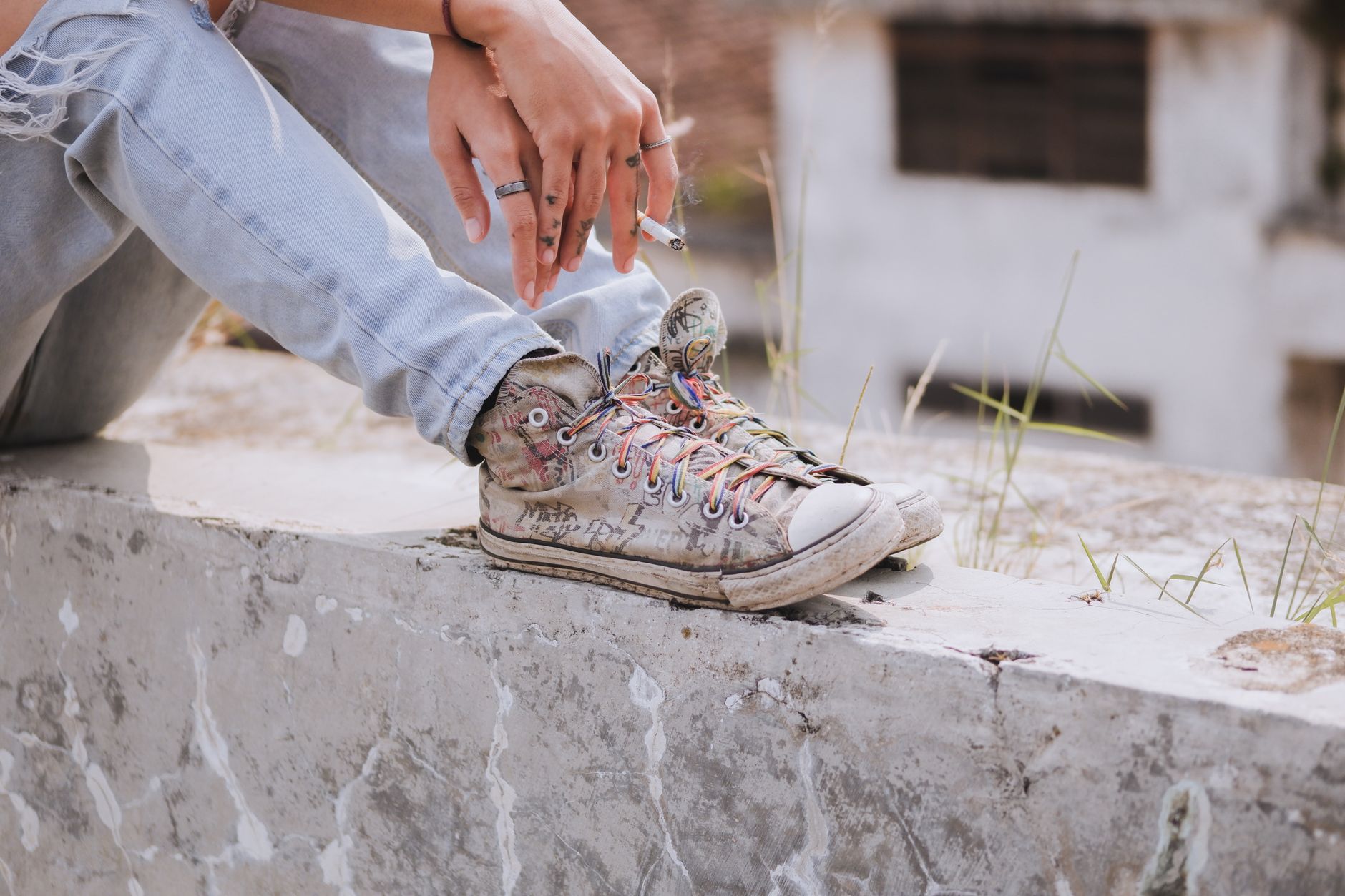 Gros plan sur une personne assise portant un jean clair déchiré et des baskets en toile décorées avec des lacets multicolores.